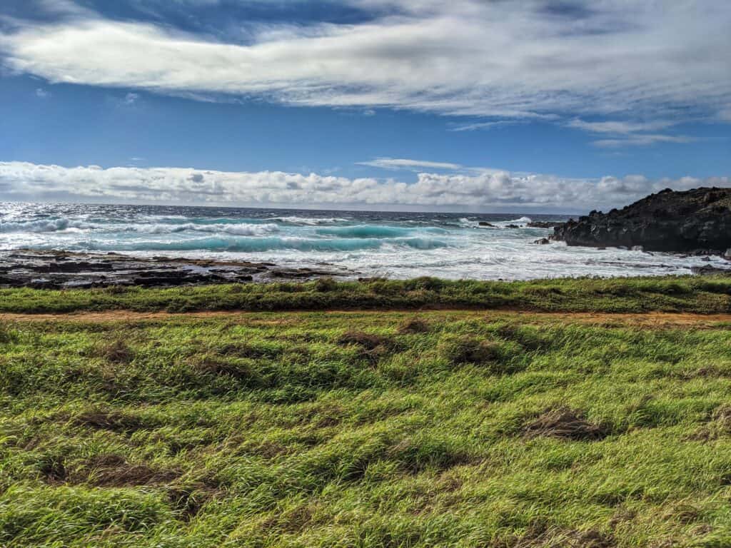 green sand beach hiking trail at south point hawaii with green grass and blue crashing waves