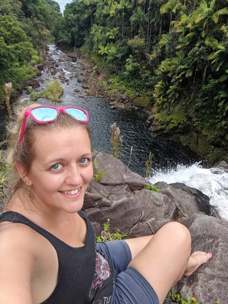 Me wearing pink sunglasses on my head, overlooking a tropical waterfall cascading into a serene pool below.