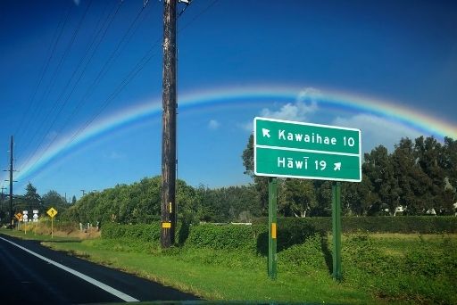 a rainbow behind a green road sign for hawi and Kawaihae