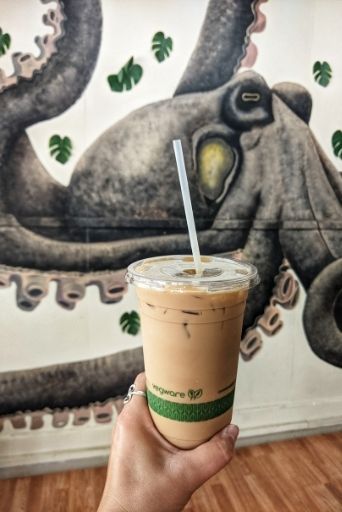 my hand holding an Iced latte from Honua's with octopus mural in the background