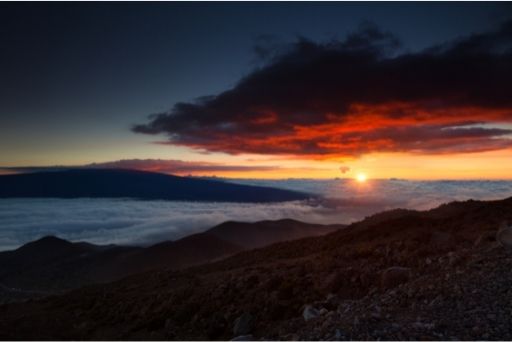 sunset on mauna kea with a valley of clouds between the mountain tops