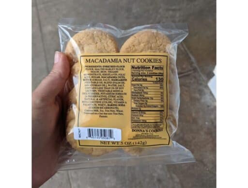 my hand holding a package of Donna's Macadamia Nut Cookies (a yummy hawaiian souvenir) with a clear view of the cookies and nutrition facts label.