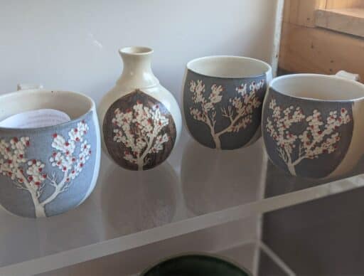 Artistic hawaiian lehua pottery on a white shelf, with delicate red and white floral patterns on a dark grey background.