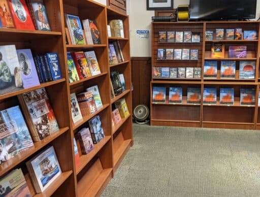 A bookshelf filled with a variety of books about Hawaiian culture, history, and landscapes, with some featuring vivid images of volcanoes.