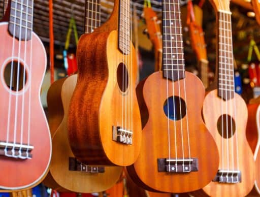 A collection of ukuleles hanging against a bright store backdrop, showing different wood finishes and sizes