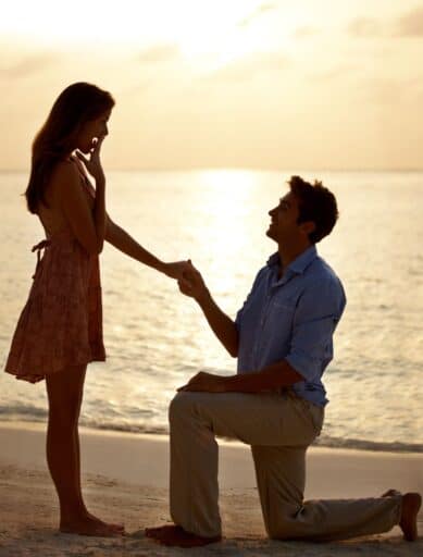 man proposing on one knee on beach at sunset