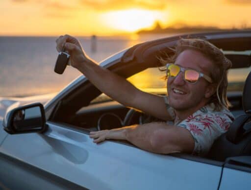 guy with sunglasses smiling out convertible with sunset behind him