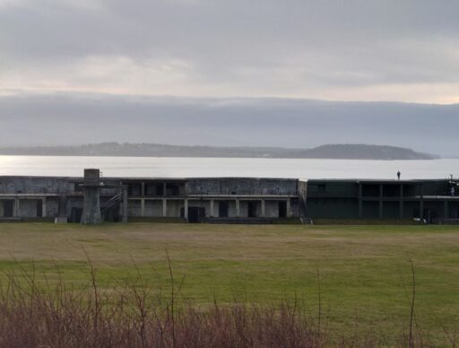Historic coastal fort with concrete bunkers and open grassy grounds overlooking the water near Coupeville under a cloudy sky. Exploring military history sites and scenic waterfront views is one of the unique things to do in Coupeville.