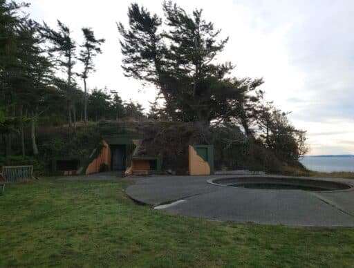 Concrete military bunker built into a grassy hillside near Coupeville with tall coastal trees and water views in the background. Exploring hidden coastal defenses and historic forts is one of the fascinating things to do in Coupeville.