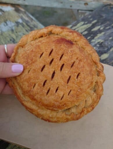 Flaky golden brown hand pie held outdoors in Coupeville with sugar crystals baked into the crust. Trying fresh baked pastries and local comfort food is one of the tasty things to do in Coupeville.