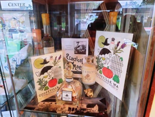 Display case inside a Coupeville gift shop filled with illustrated cards, perfume bottles, and local souvenirs. One card reads "Coupeville WA It's Practically Magic," highlighting the small town shopping experiences and local finds among the things to do in Coupeville.