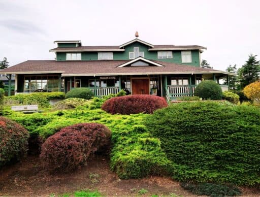 Large green historic building surrounded by neatly trimmed shrubs and gardens in Coupeville. Visiting local museums and learning about Whidbey Island history is one of the educational things to do in Coupeville.