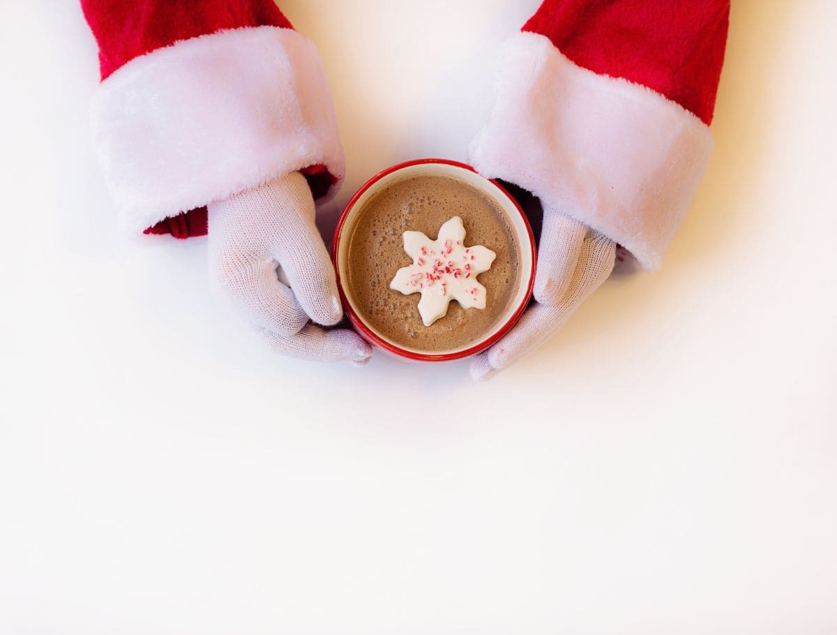 view looking down on santa hands holding a mug of hot chocolate witha snowflake shaped marshmallow