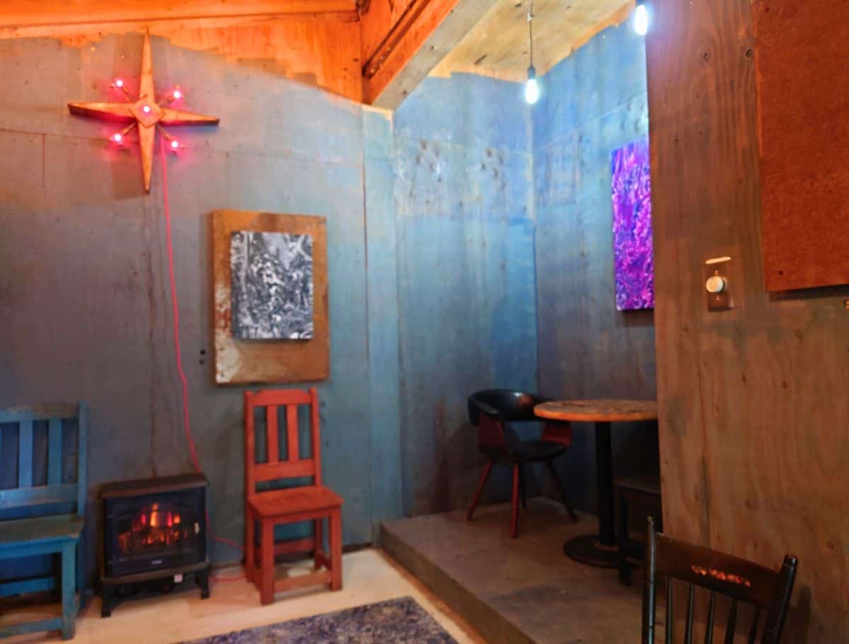 Cozy lounge area inside a Whidbey Island coffee shop with warm lighting, colorful chairs, local artwork, and a small fireplace creating an intimate atmosphere. Unique spaces to relax with handcrafted drinks help make this one of the best coffee spots on Whidbey Island.