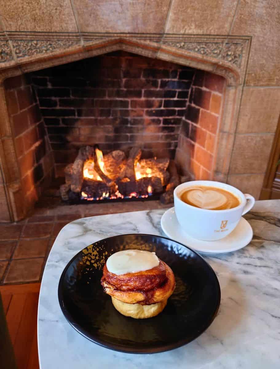 macrina bakery cinnamon roll and cup of muse latte in front of the fireplace