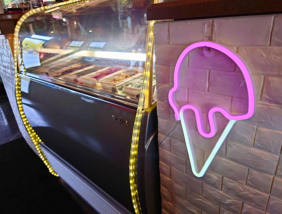 Neon pink ice cream cone sign glowing beside a lit dessert display case inside a modern café on Whidbey Island. Trendy cafés with pastries and sweet treats often serve some of the best coffee on Whidbey Island.