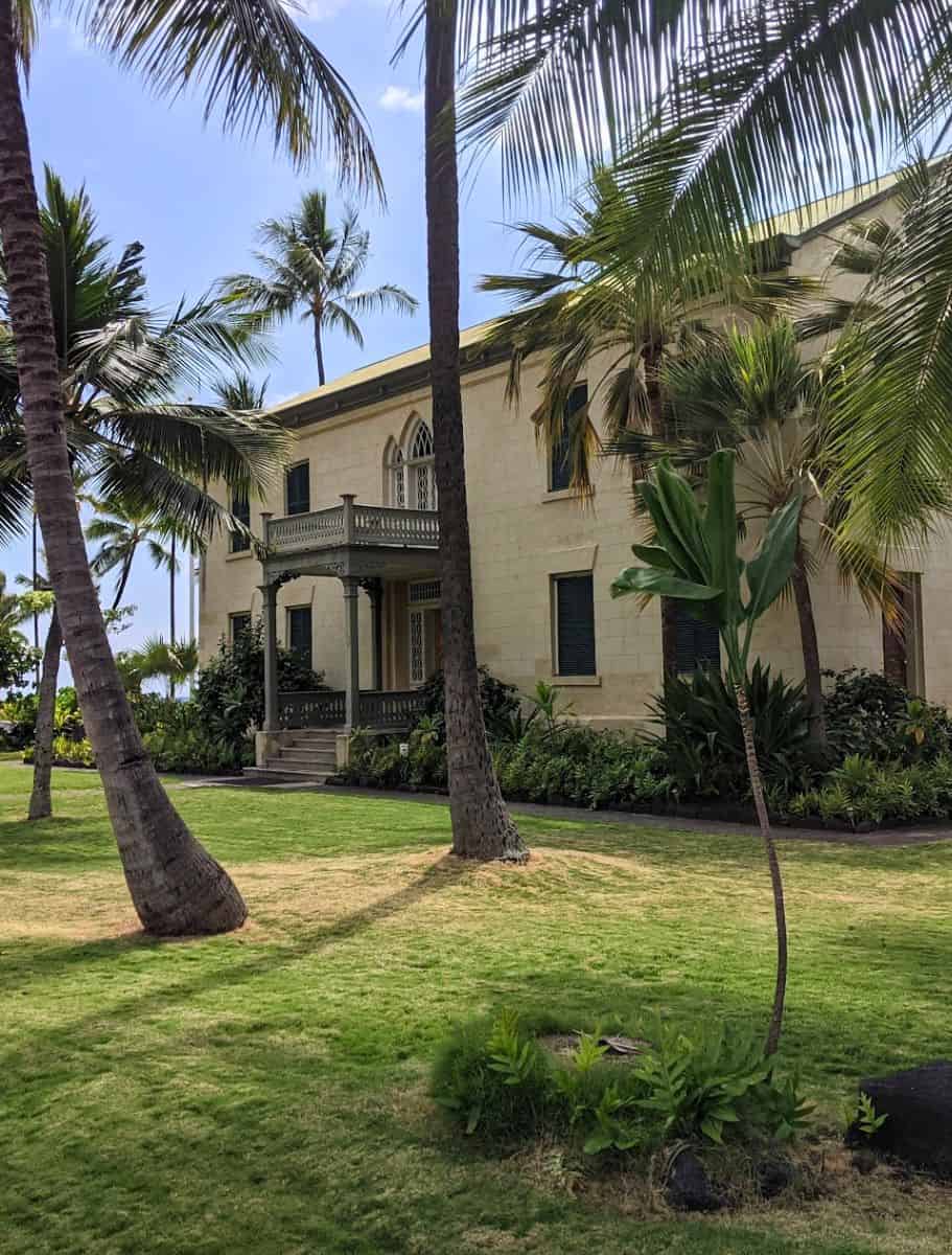 Historic Hulihe'e Palace framed by tropical palms on the Big Island, inviting visitors to explore Hawaiian heritage even in rainy weather.