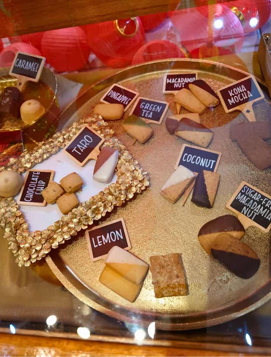 Assortment of Hawaiian shortbread cookies, some dipped in chocolate, displayed on a golden tray, tempting visitors at big island candies