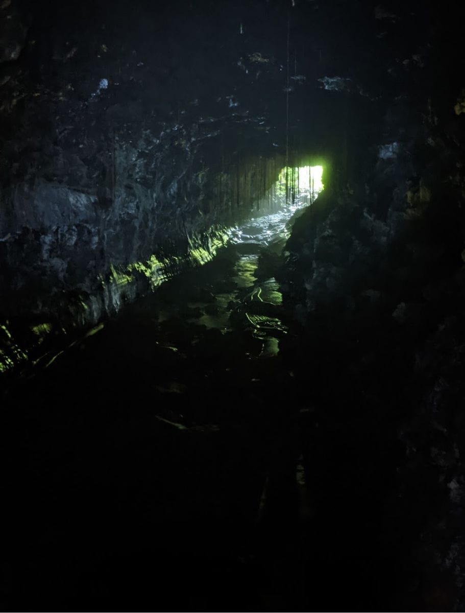 A dim view inside the Kaumana Caves with a faint light illuminating the wet cave walls and floor, creating a serene and mysterious atmosphere