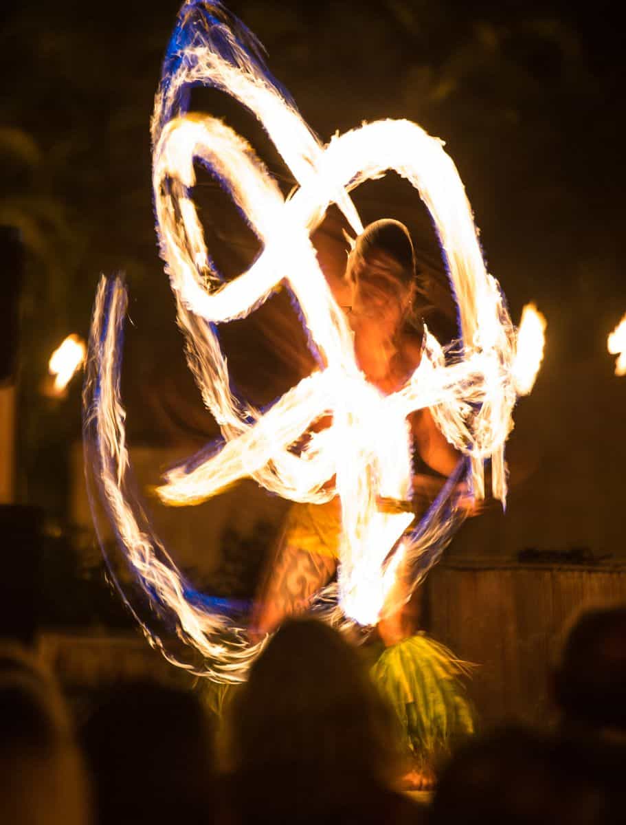A vibrant fire dancer performing at night, with blurred motion flames, showcasing traditional Hawaiian entertainment.