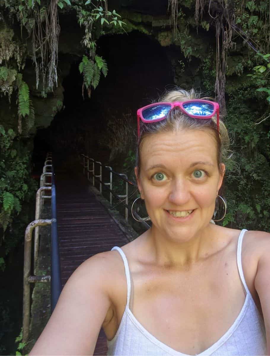 selfie of me making a funny face in front of the shadowy entrance to the Thurston Lava Tube, surrounded by lush ferns and foliage,