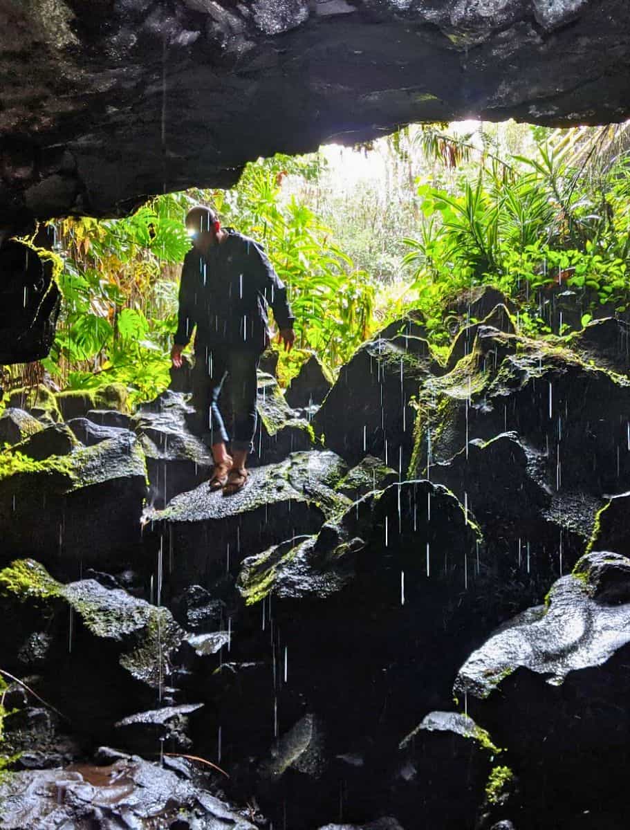 michael in a rain jacket and headlamp stands silhouetted against the bright cave exit, with water droplets visible in the air