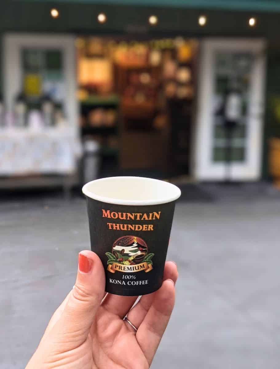A close-up of my hand holding a sample cup of Mountain Thunder Kona coffee,