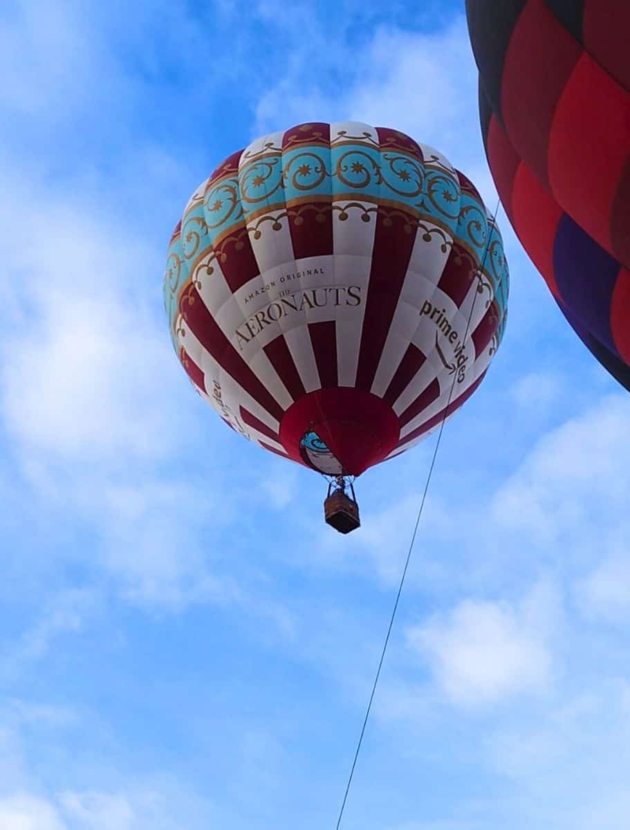 A hot air balloon adorned with intricate patterns and labeled 'Aeronauts' floats in a clear blue sky.