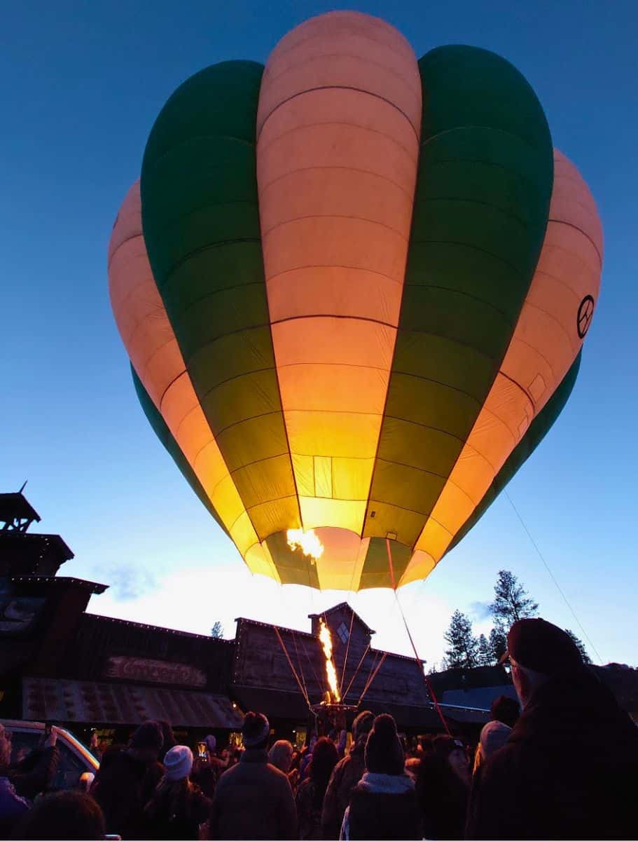 A hot air balloon glowing warmly against a dusk sky, with the flame heating the balloon as onlookers gather in the twilight.