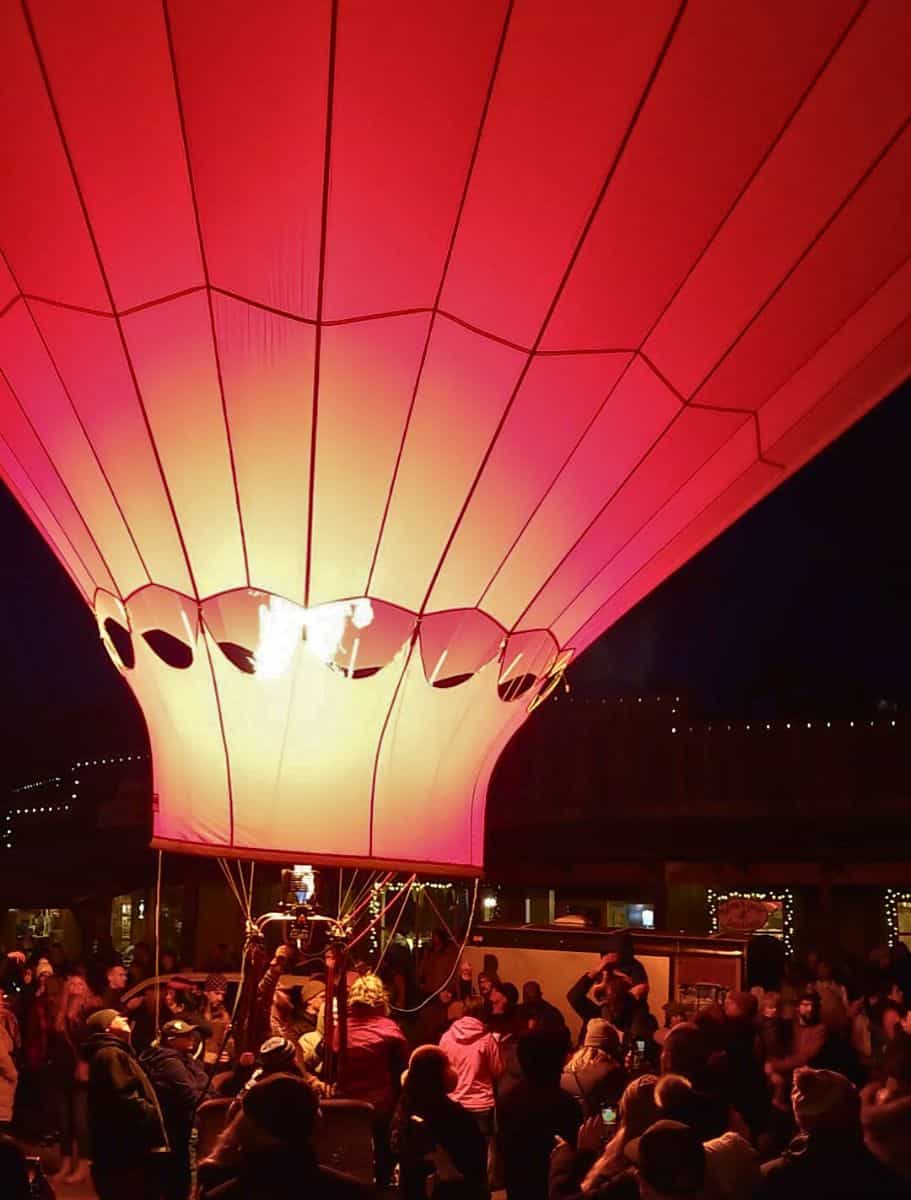 A red hot air balloon illuminated from within, casting a vibrant glow over the crowd of spectators during the winthrop balloon roundup glow up
