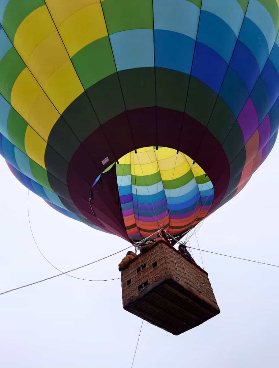View from beneath a hot air balloon, focusing on the woven basket and the colorful envelope above