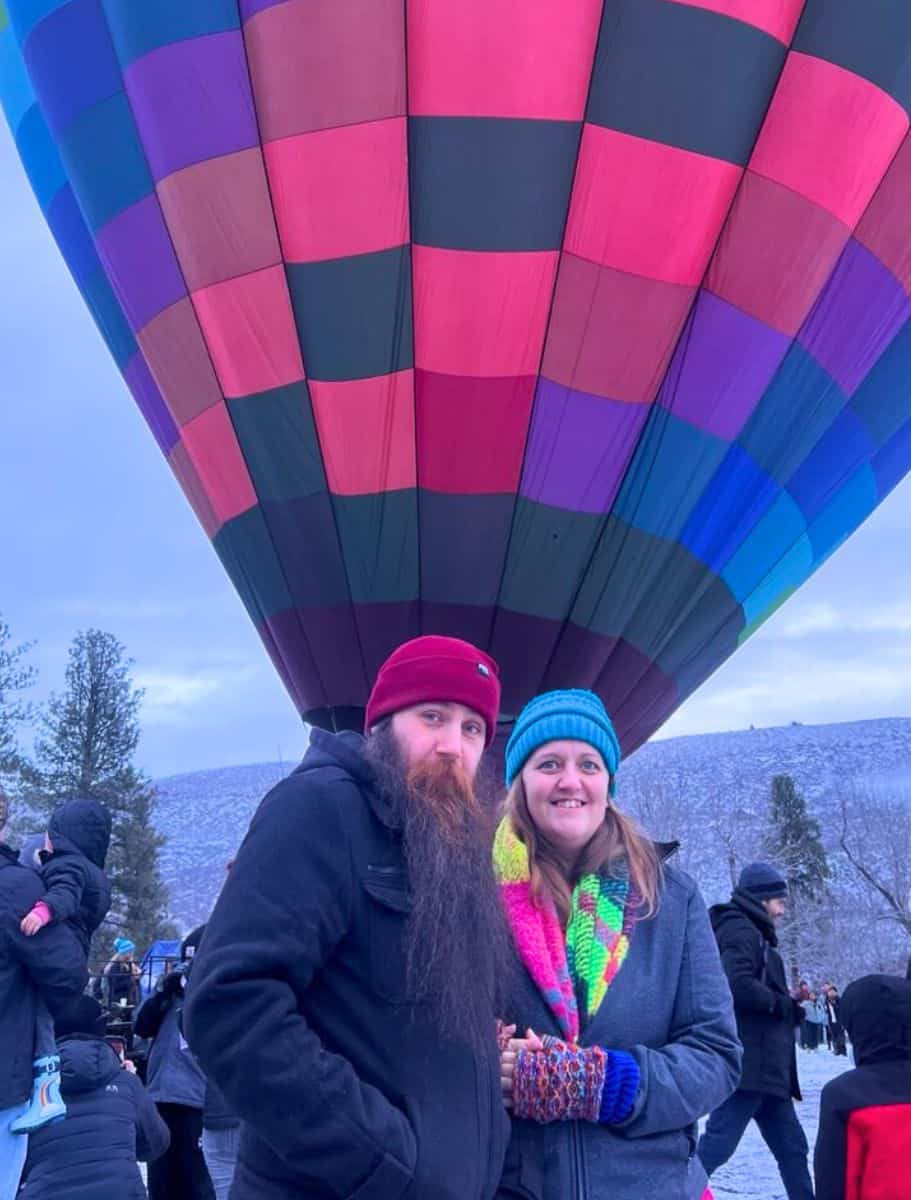 michael and i in our winter hats and scarfs in front of a partially obscured hot air balloon, with a wintry landscape in the background