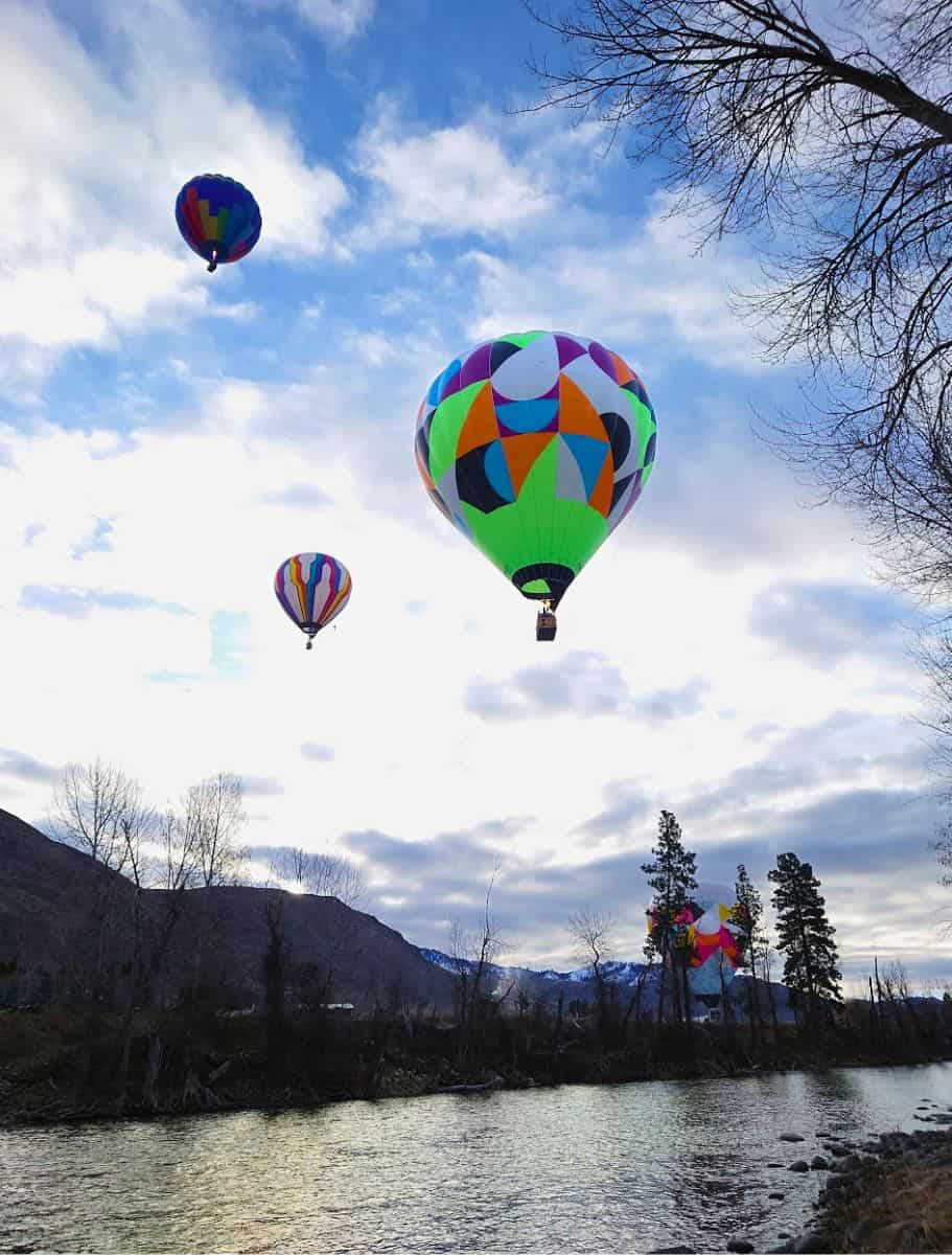 Several colorful hot air balloons float above a the river,
