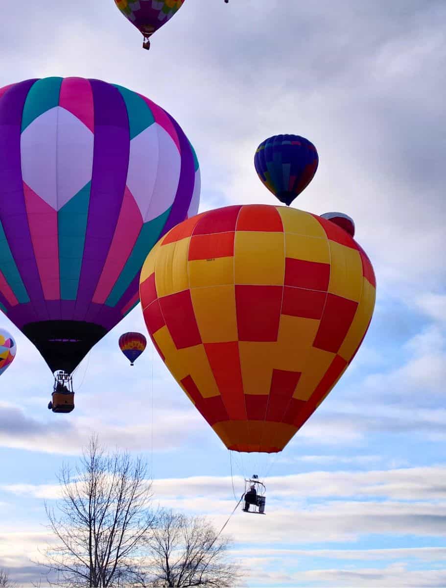 large hot air balloons hovering, one without a basket, against a cloudy sky,