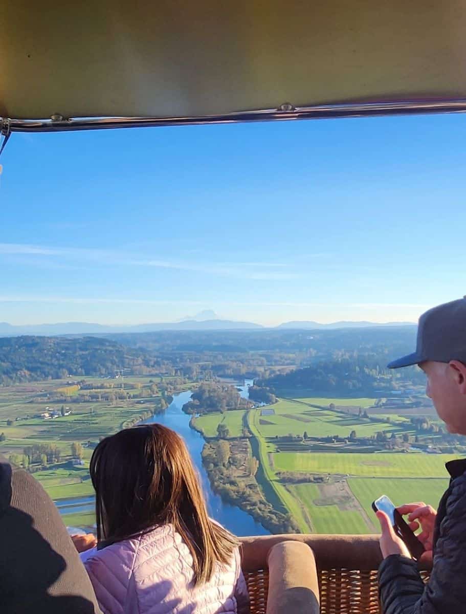 Passengers in a hot air balloon basket enjoying a panoramic view of the Snohomish landscape, rivers, and fields below.