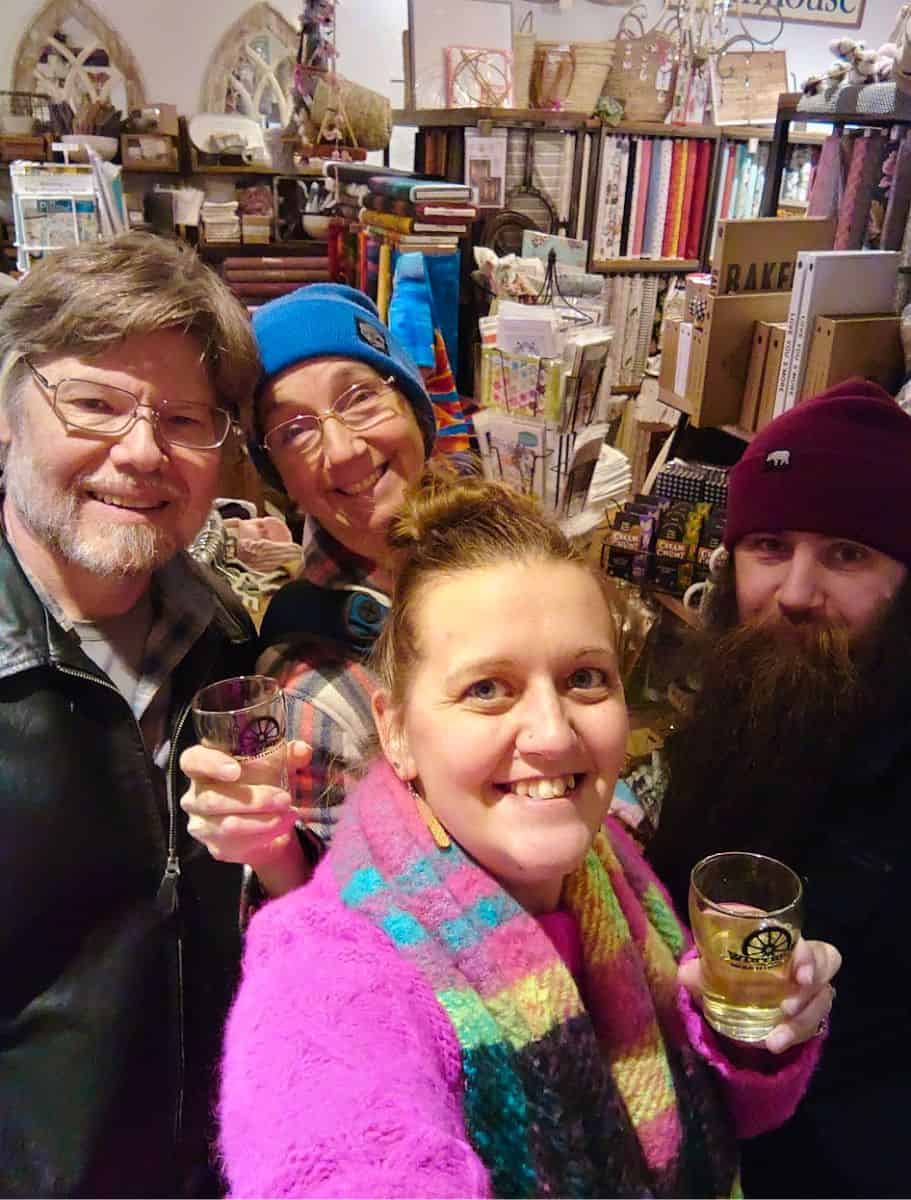 the four of us taking a group selfie featuring toasting with small glasses of wine inside a cozy craft store during the Winthrop sip and stroll event