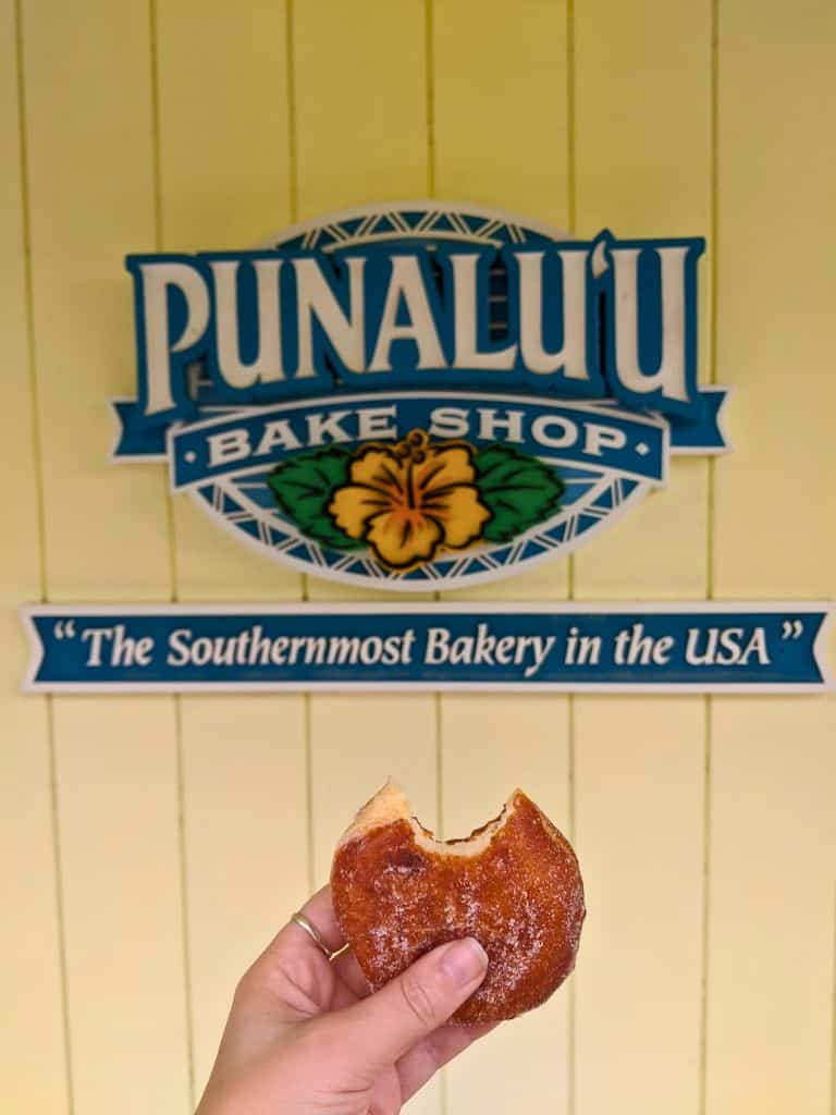 my holding a Traditional malasada from Punalu'u Bake Shop with a bite taken out