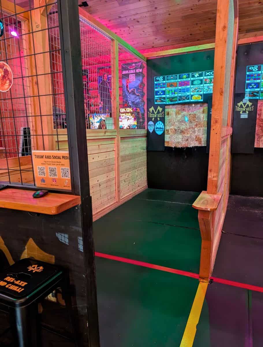 Indoor axe throwing lanes with wooden targets, neon lighting, and fenced throwing areas inside an entertainment venue in Oak Harbor. Trying axe throwing with friends is one of the adventurous things to do in Oak Harbor for a fun night out.