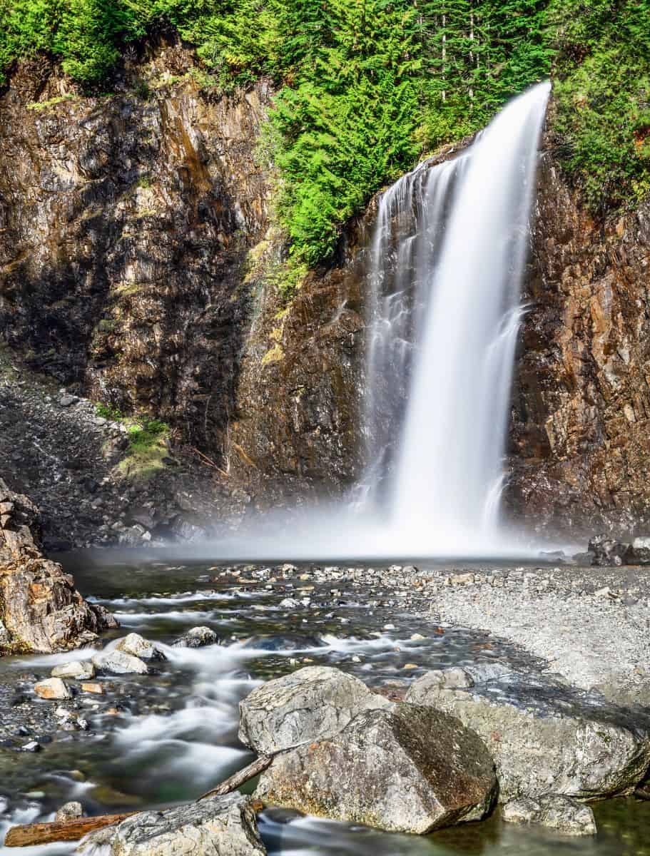 Franklin Falls cascading into shallow rocky pool below. cliffs at top are topped with evergreen forest