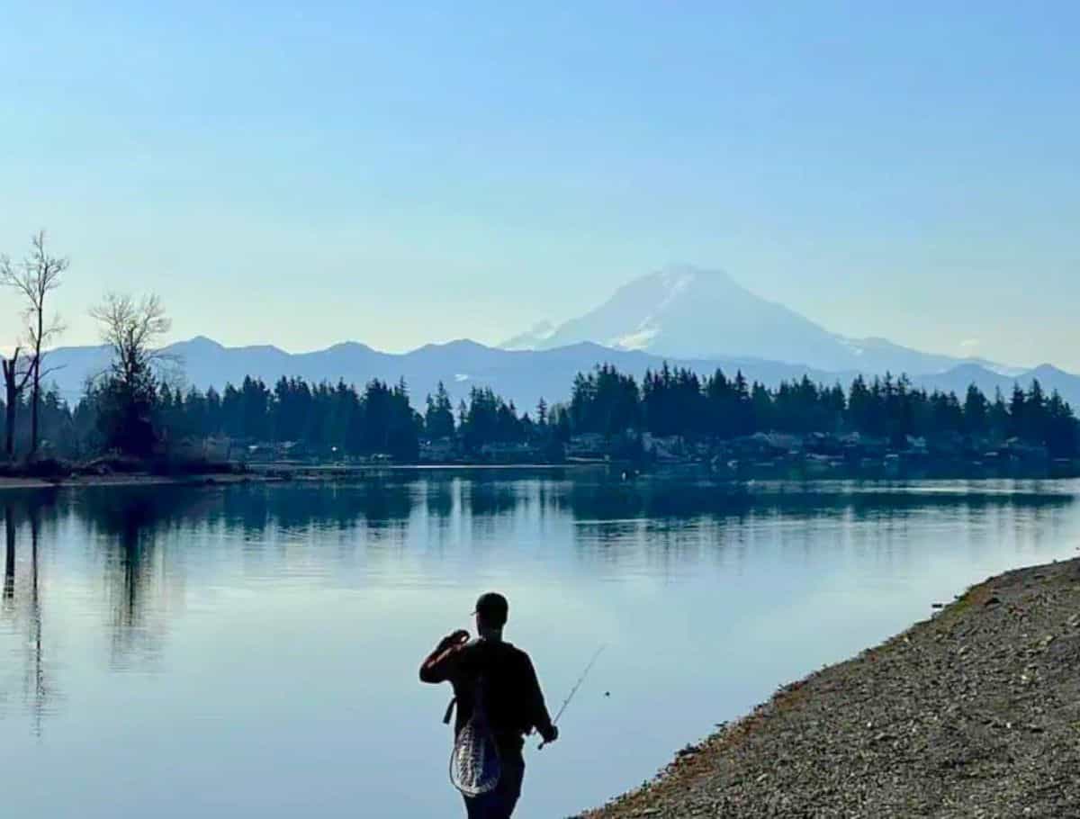 fishman silhouetted in foreground. lake tapps with smooth waters and mt rainier looming in the background