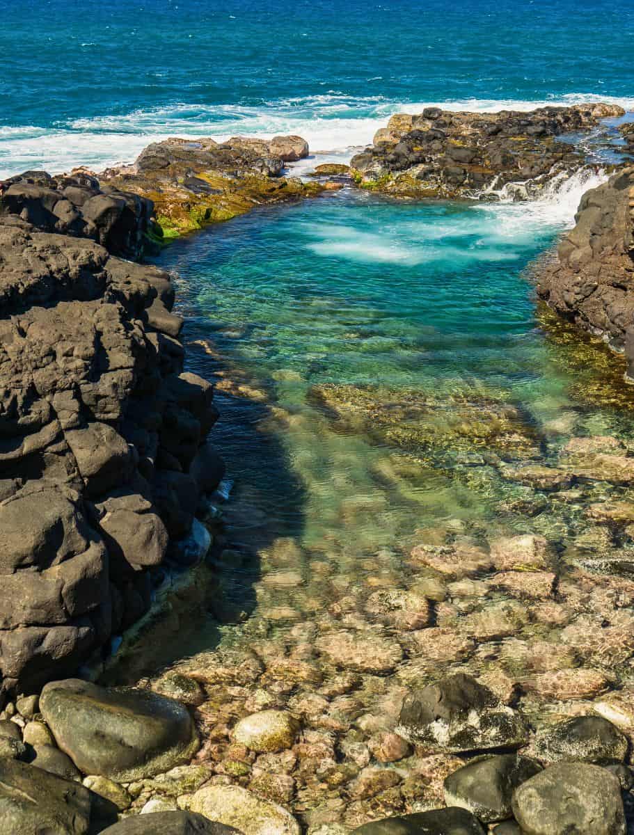 queens bath, a natural pool by ocean full of blue water, surrounded by lava rock and ocean water filling the pool