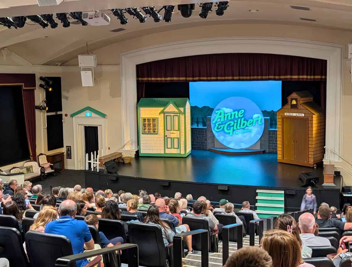 The set for Anne & Gilbert: The Musical; a green gabled shed and schoolhouse shed; with audience filling the seats
