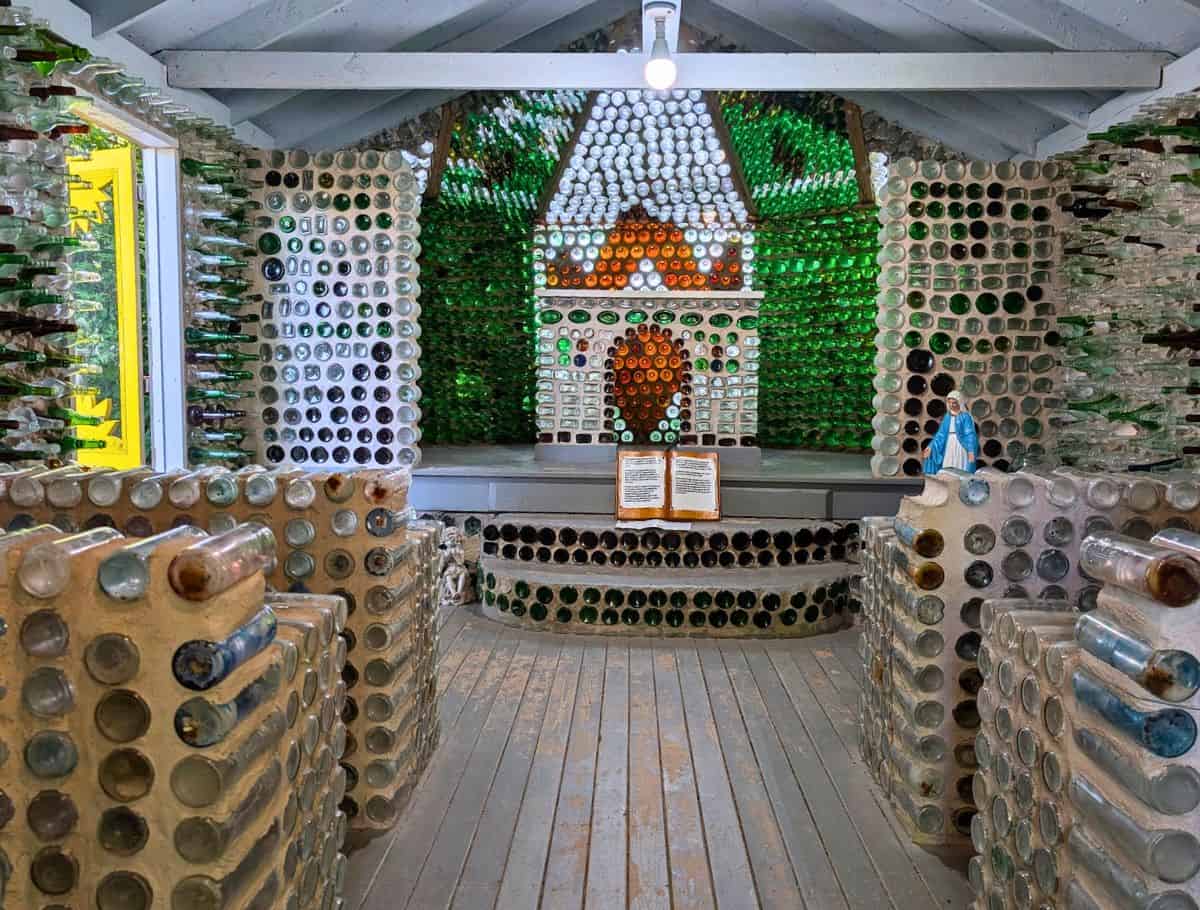 inside The Glass Bottle Houses and Gardens chapel with pews and walls and altar made of glass bottles