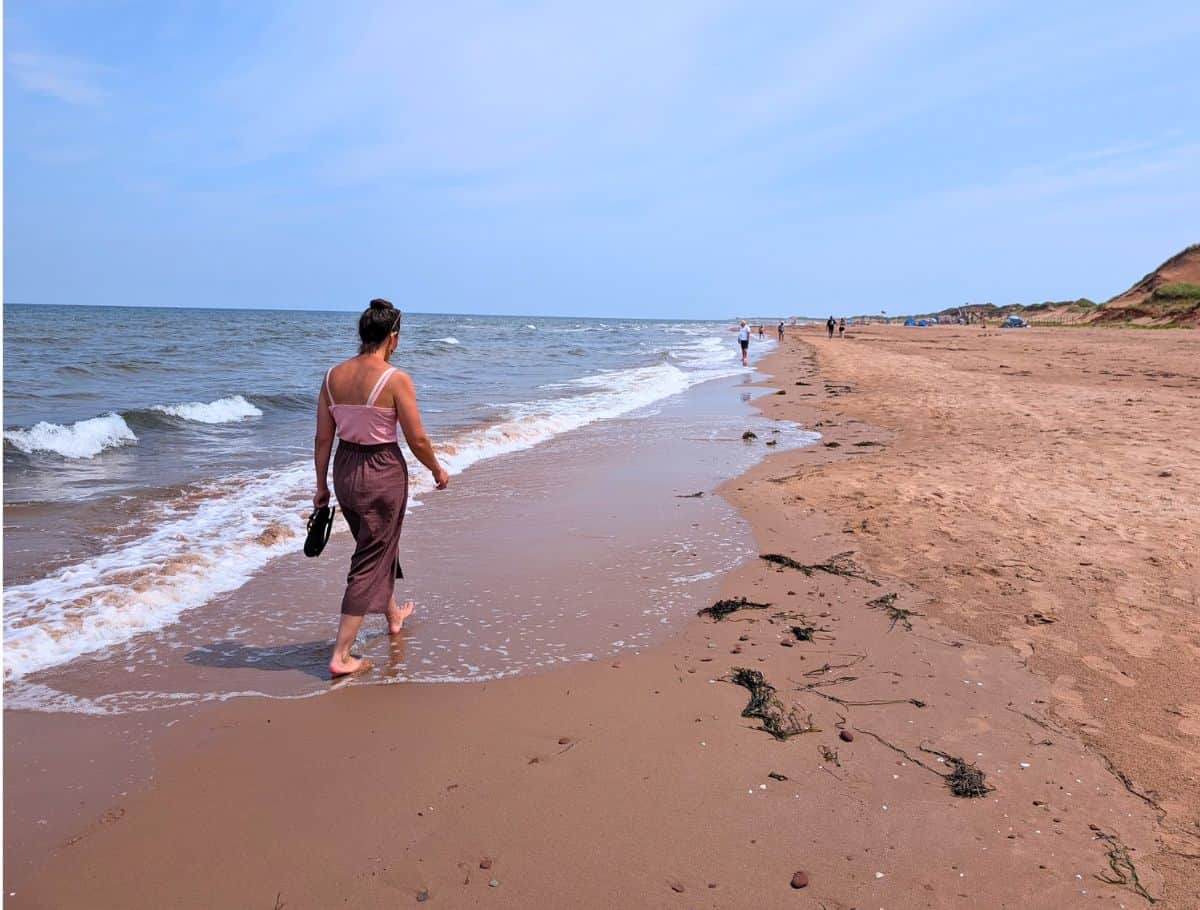 woman walking barefoot along shoreline on Brackley Beach