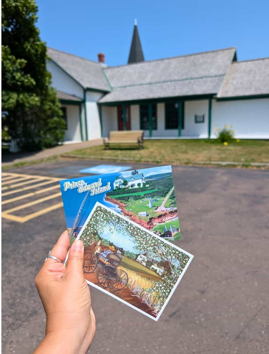 my hand holding PEI postcards in front of the Cavendish post office