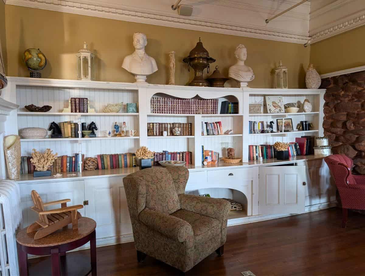 wall of white shelves with books lining it and some wing back chairs