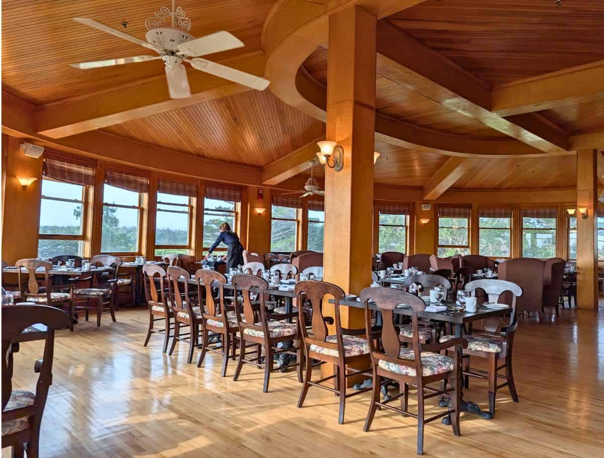 Circular dining room filled with long tables and a wall of windows overlooking the property
