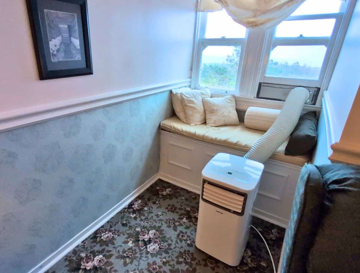 ac unit on floor with hose coming out of window over the window bench