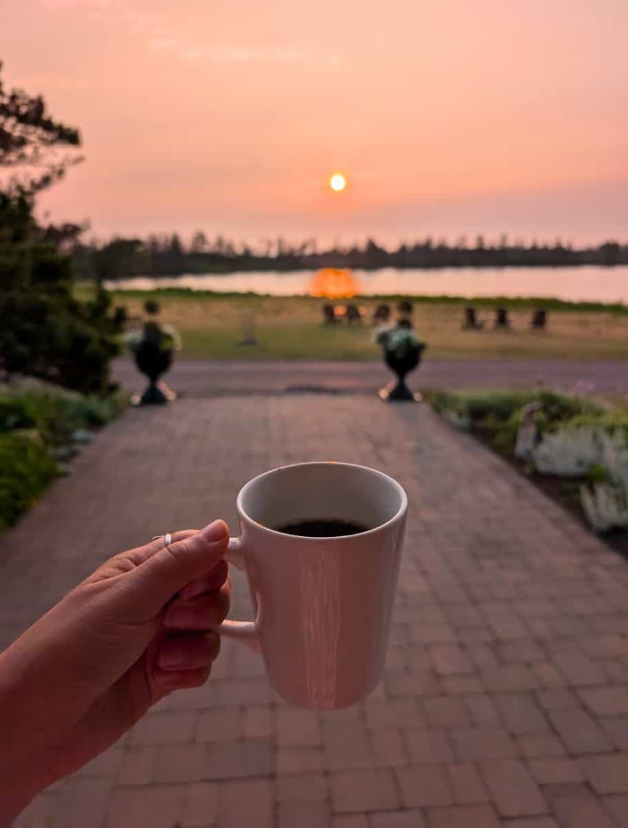 my hand holding a cup of coffee overlooking the lake at sunrise