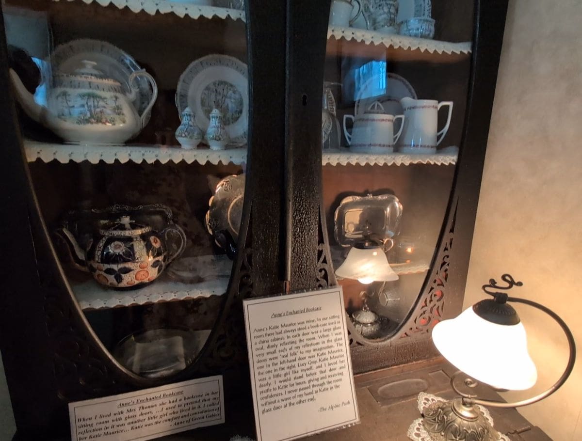 The enchanted bookcase inspiration for Anne of Green Gables with windows looking at china sets and a lit lamp on the desk